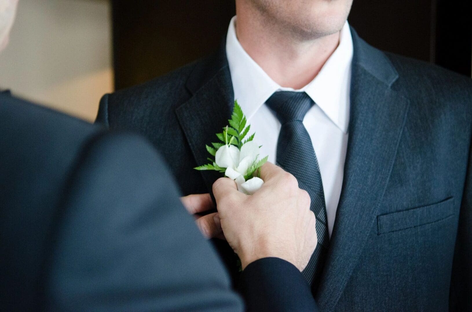 A man in suit and tie fixing another mans flower.